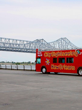 Red double-decker bus for city sightseeing in New Orleans near a steel bridge.