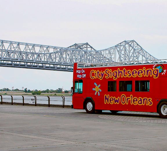 Red double-decker bus for city sightseeing in New Orleans near a steel bridge.
