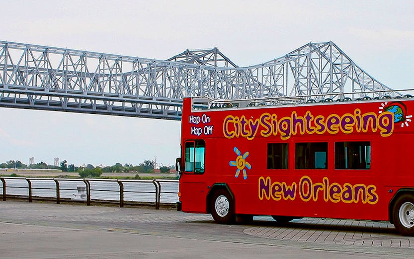 Red double-decker bus for city sightseeing in New Orleans near a steel bridge.