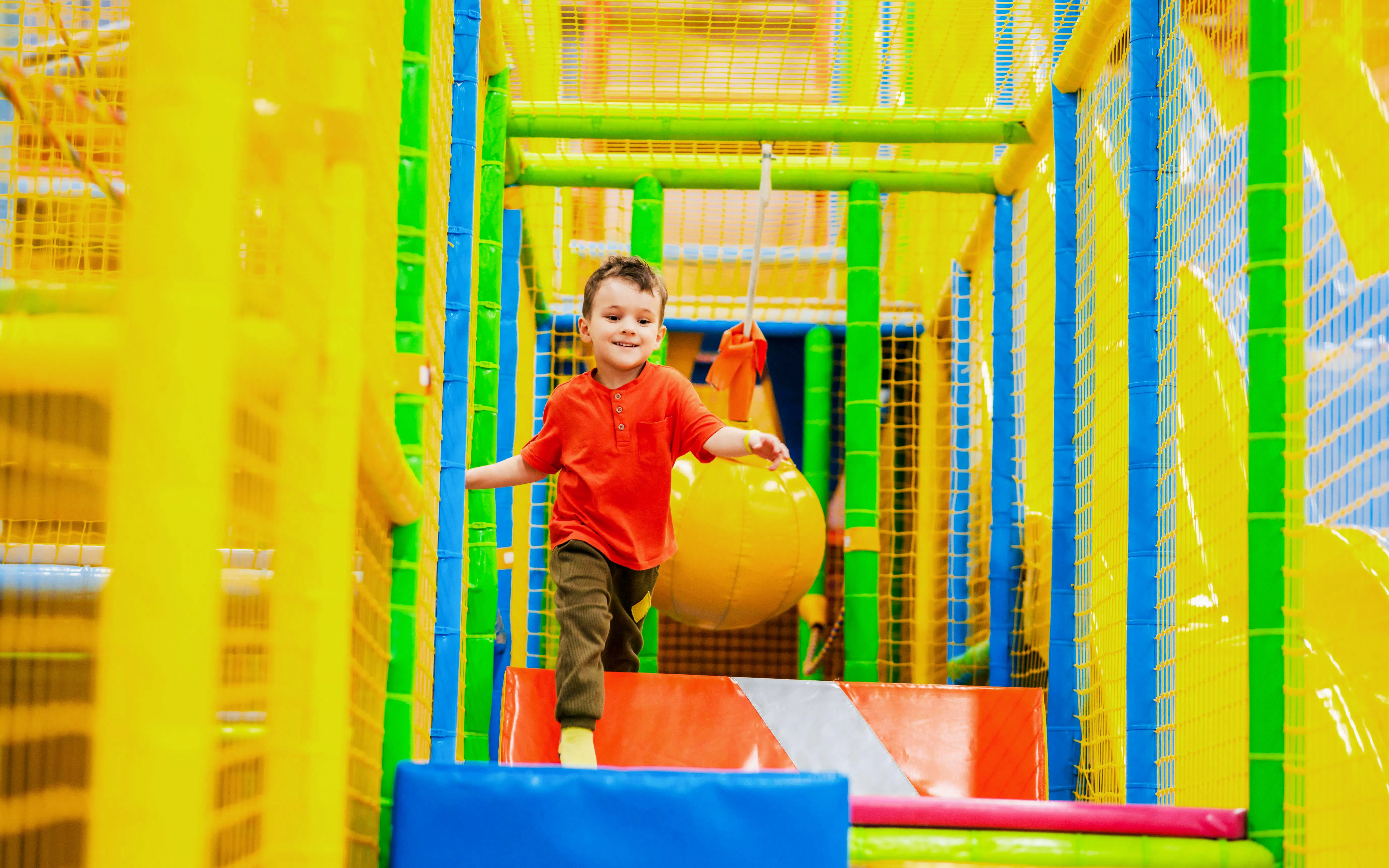 Child playing in colorful indoor play area with climbing structures.