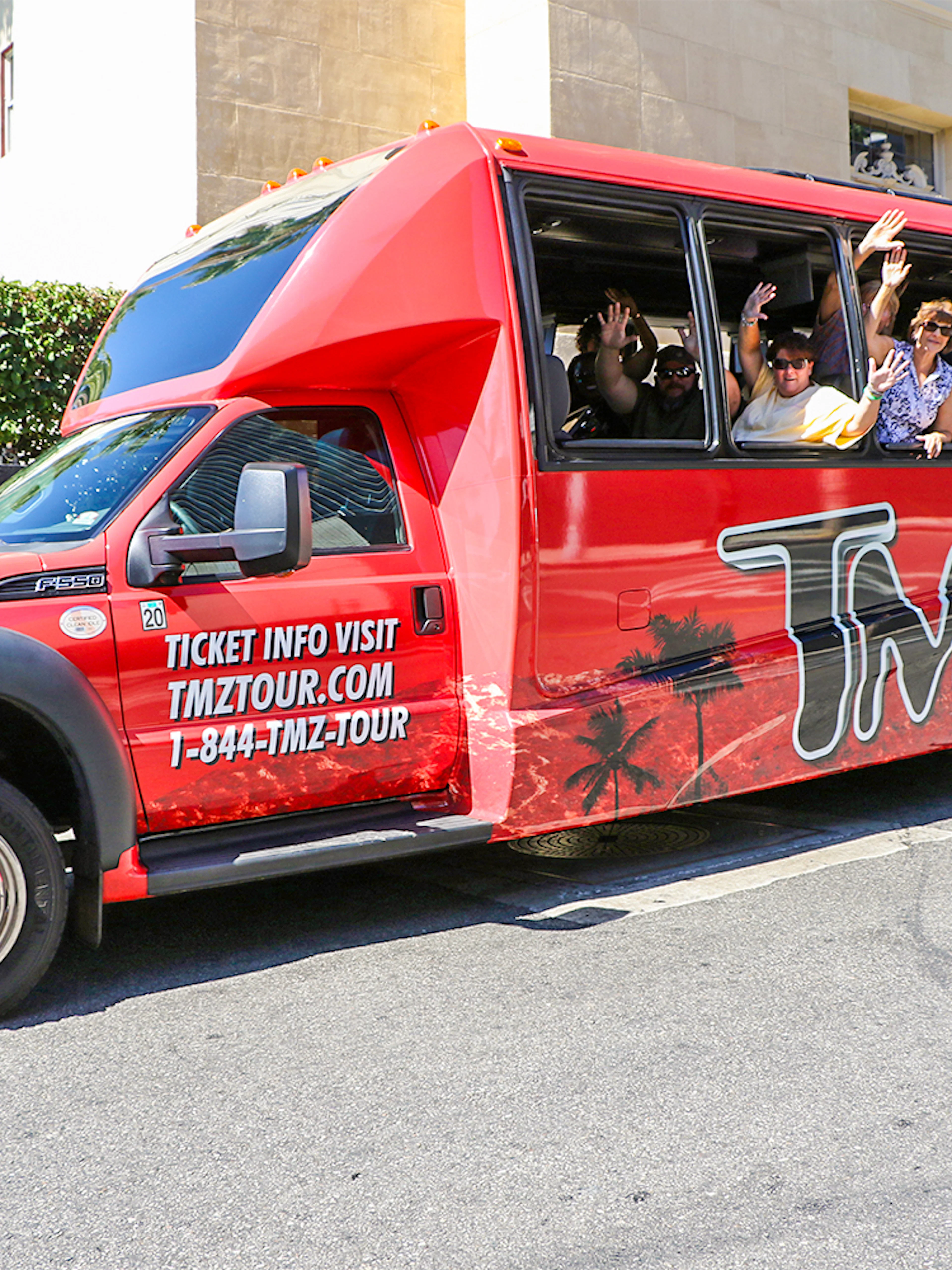 TMZ tour bus with passengers waving on Hollywood street.