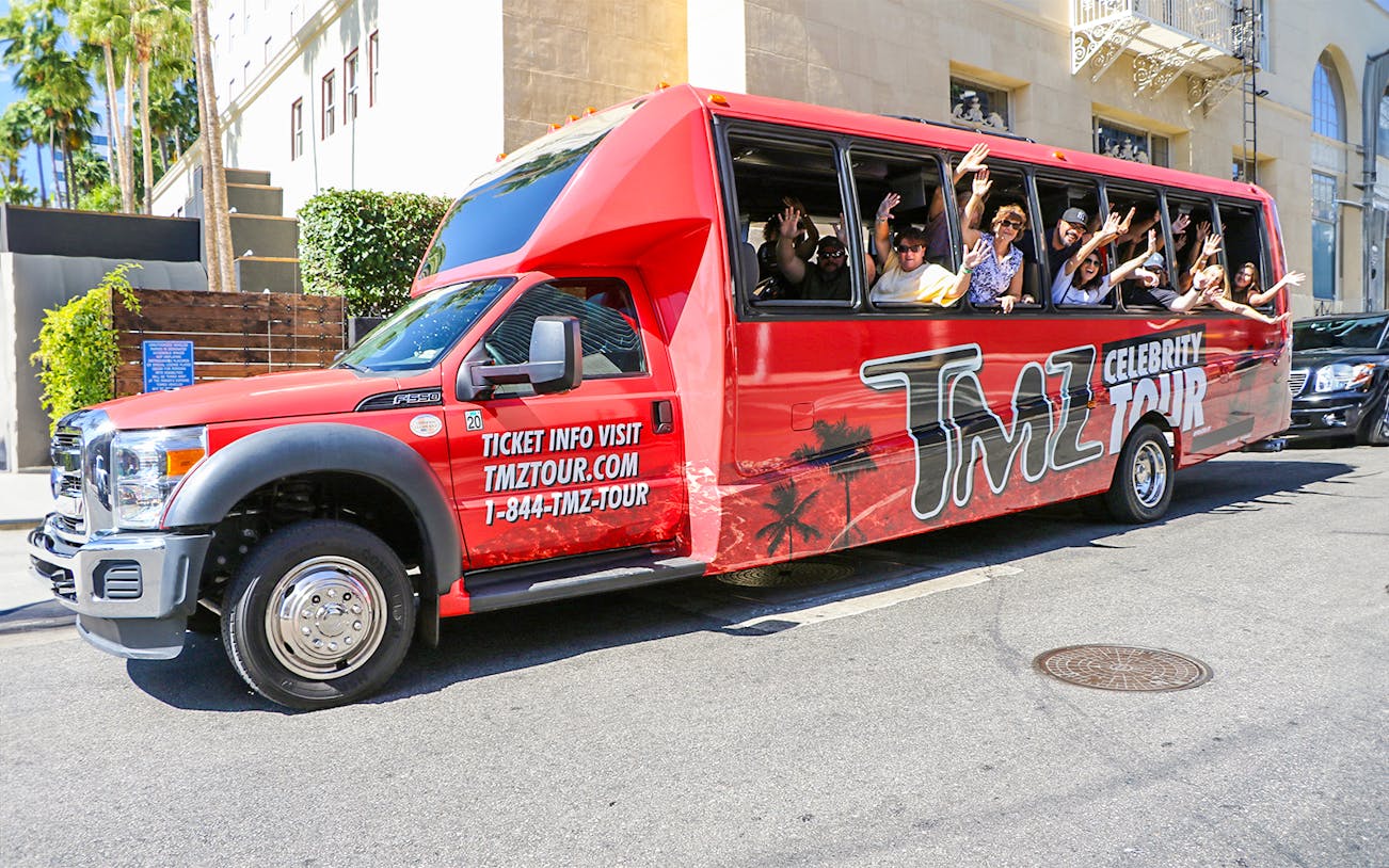 TMZ tour bus with passengers waving on Hollywood street.