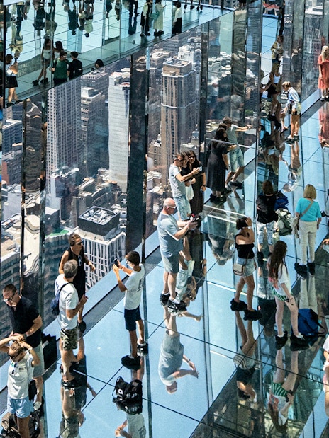 Visitors walking on glass floors at SUMMIT One Vanderbilt, New York City, with skyline reflections.