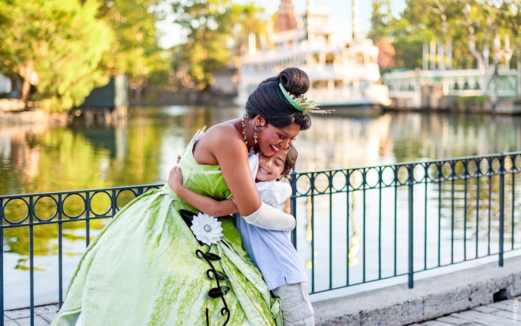 Child hugging a princess at Disneyland Park, California, near a waterfront.
