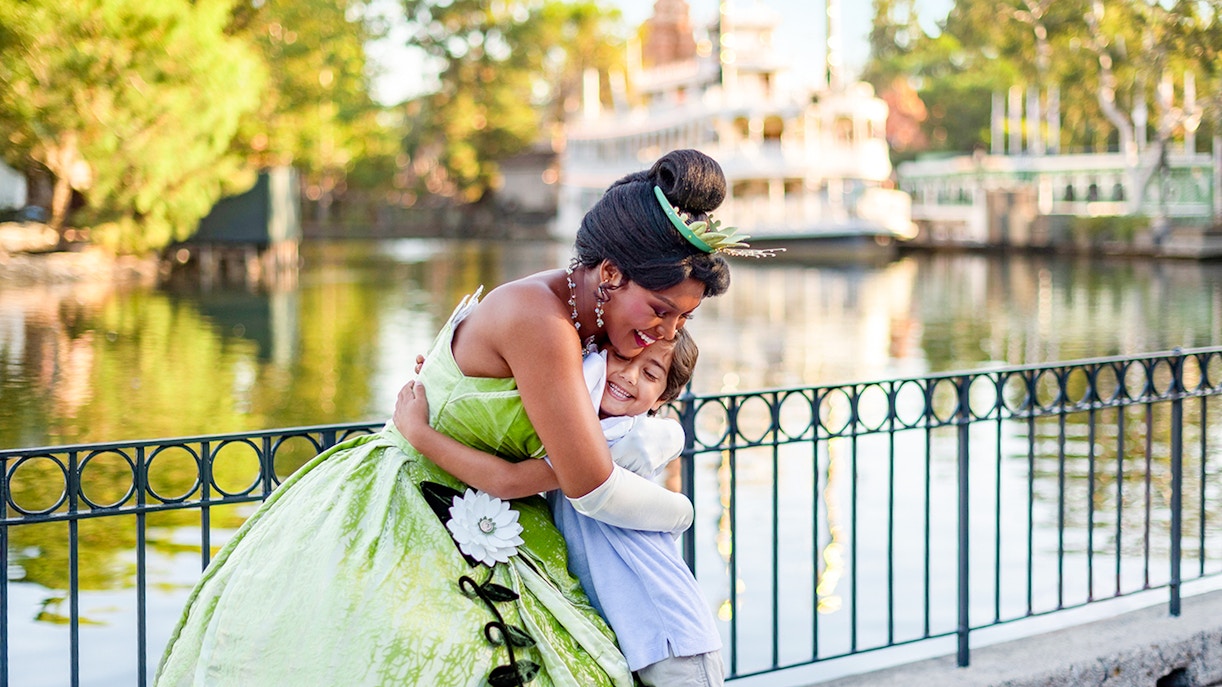 Child hugging a princess at Disneyland Park, California, near a waterfront.