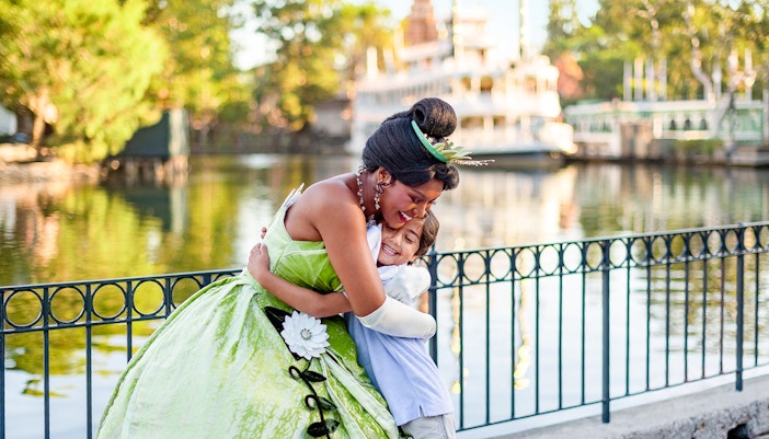 Child hugging a princess at Disneyland Park, California, near a waterfront.