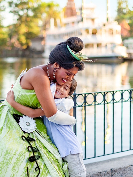 Child hugging a princess at Disneyland Park, California, near a waterfront.