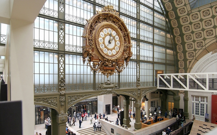 Vintage railway station clock inside a grand hall with people exploring.