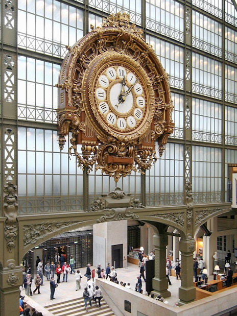 Vintage railway station clock inside a grand hall with people exploring.