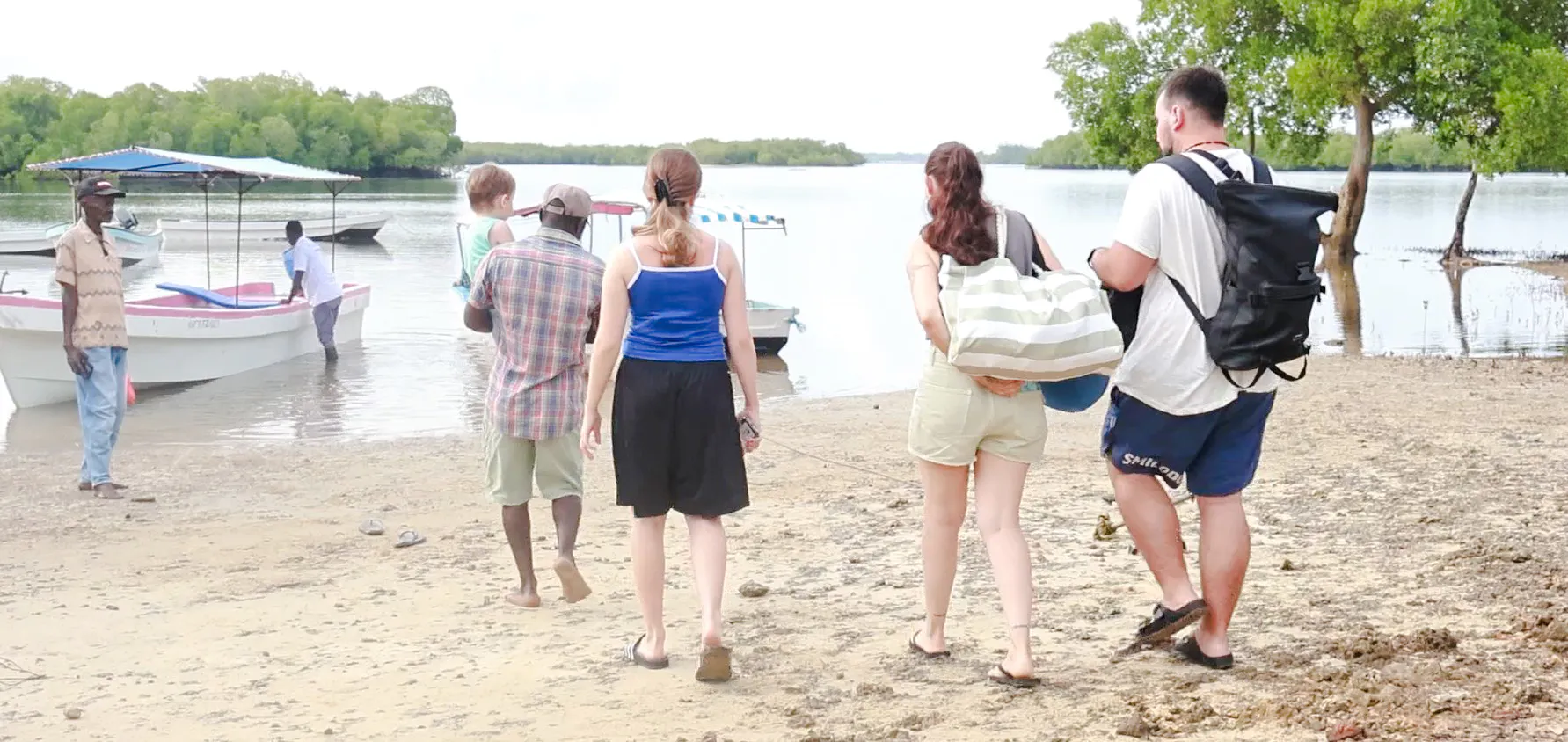 Tourists walking on a sandy beach towards a boat for Funzi Island excursion from Diani Beach.