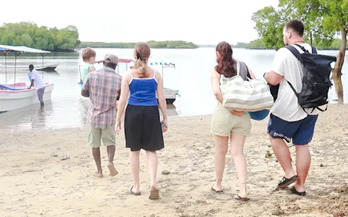 Tourists walking on a sandy beach towards a boat for Funzi Island excursion from Diani Beach.