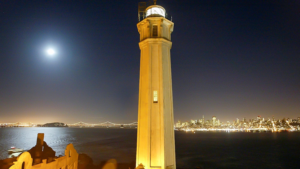 Alcatraz Island lighthouse with San Francisco skyline at night.
