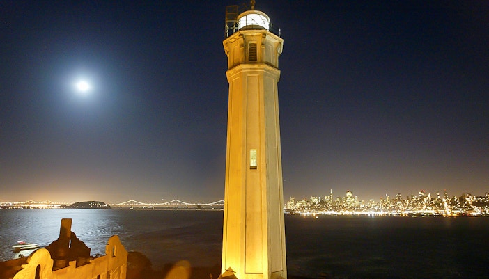 Alcatraz Island lighthouse with San Francisco skyline at night.