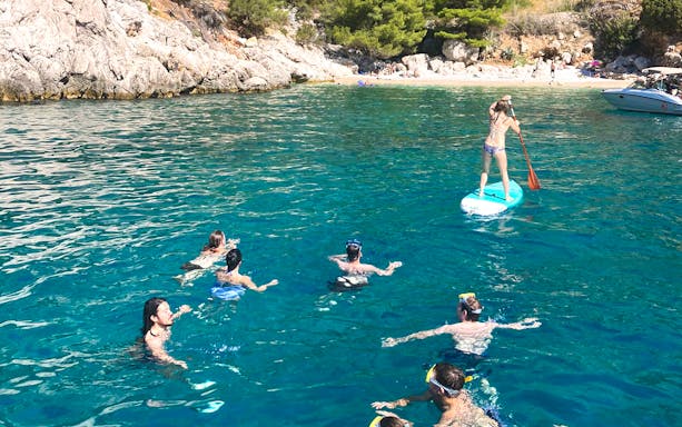 People swimming and paddleboarding near a rocky beach in Hvar during a yacht tour.