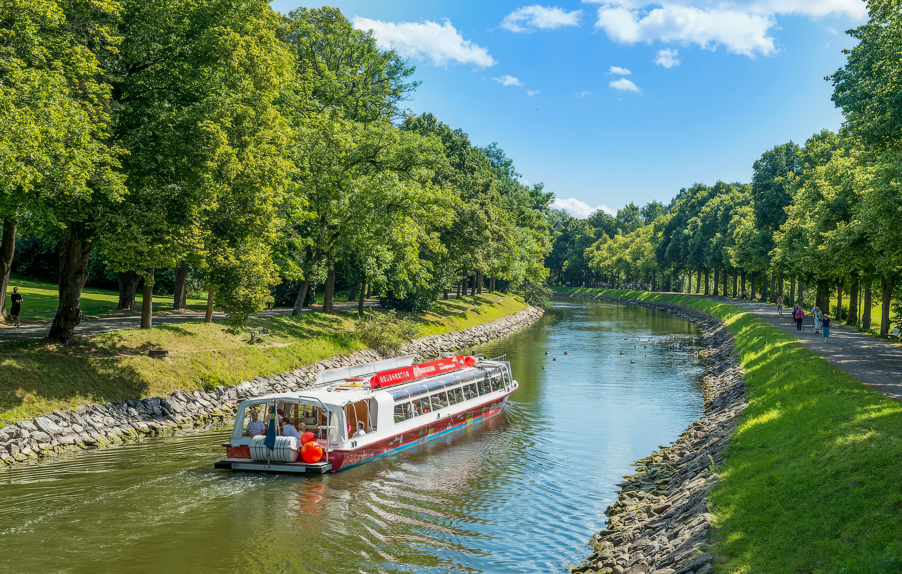 Sightseeing boat on Djurgarden Canal in Stockholm, Sweden, surrounded by lush greenery.