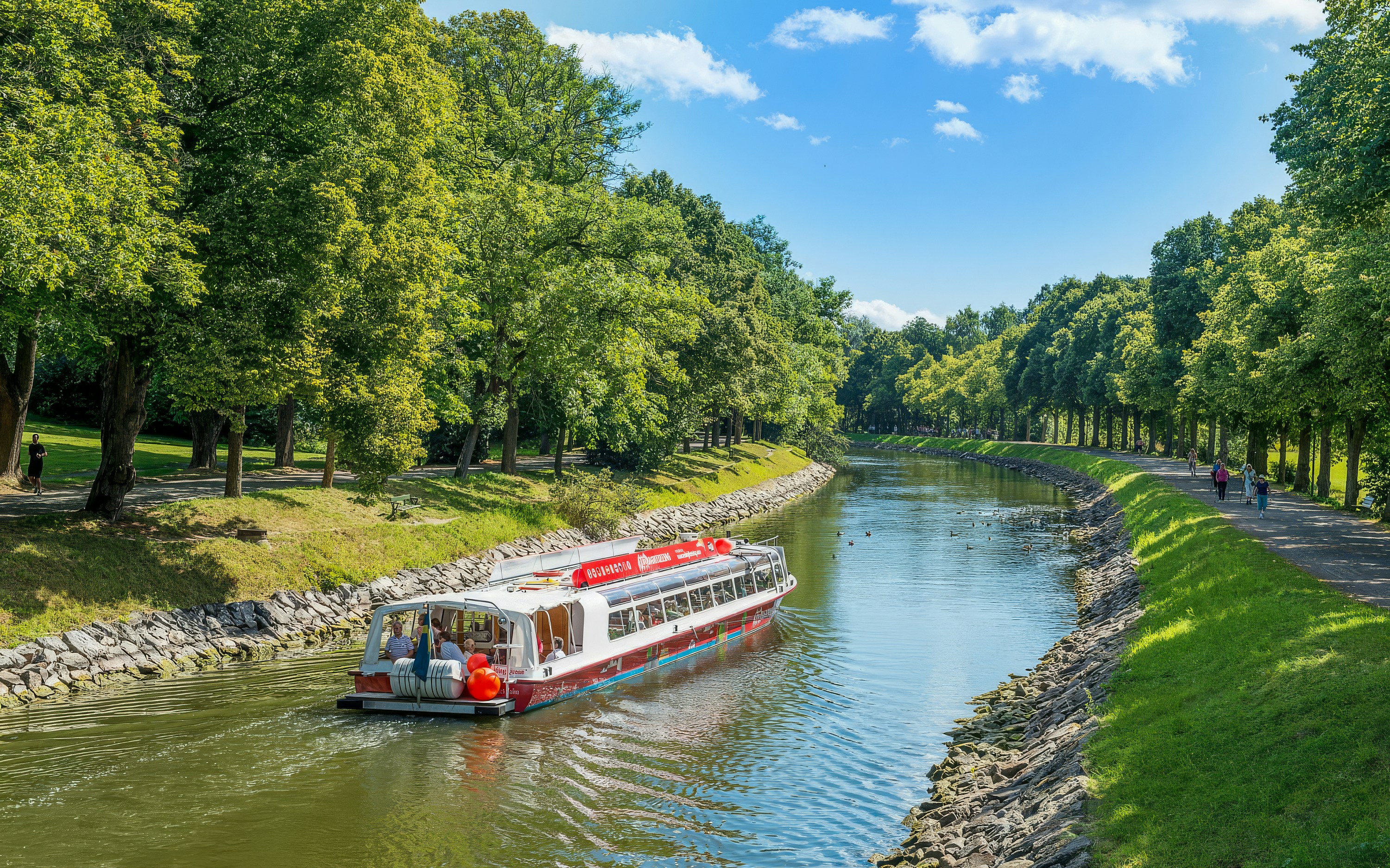 Sightseeing boat on Djurgarden Canal in Stockholm, Sweden, surrounded by lush greenery.