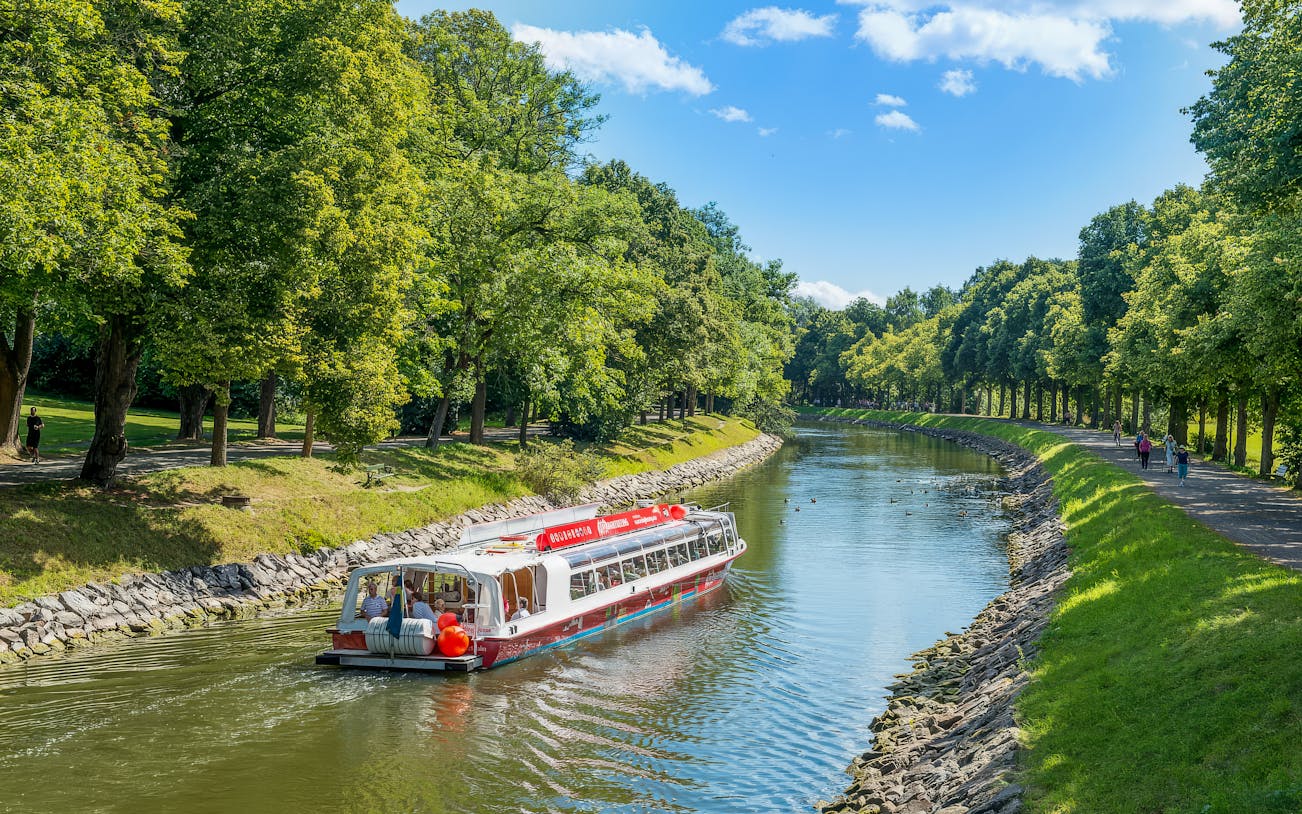 Sightseeing boat on Djurgarden Canal in Stockholm, Sweden, surrounded by lush greenery.