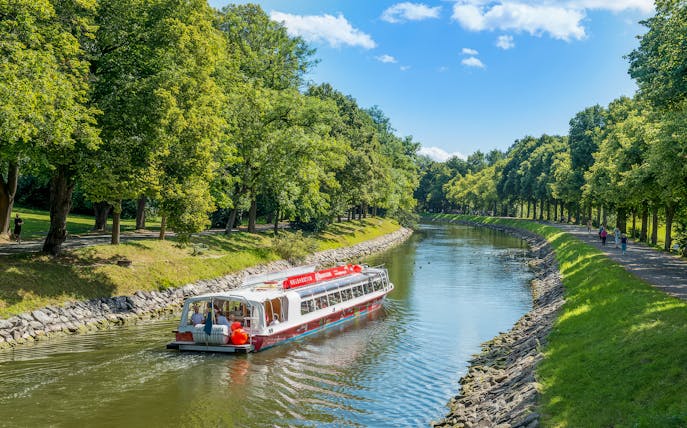 Sightseeing boat on Djurgarden Canal in Stockholm, Sweden, surrounded by lush greenery.