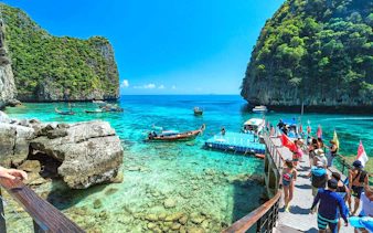 Tourists boarding a speedboat at a dock with clear waters and limestone cliffs in Phi Phi Islands, Phuket.