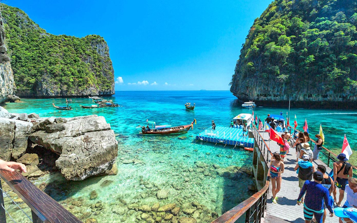 Tourists boarding a speedboat at a dock with clear waters and limestone cliffs in Phi Phi Islands, Phuket.