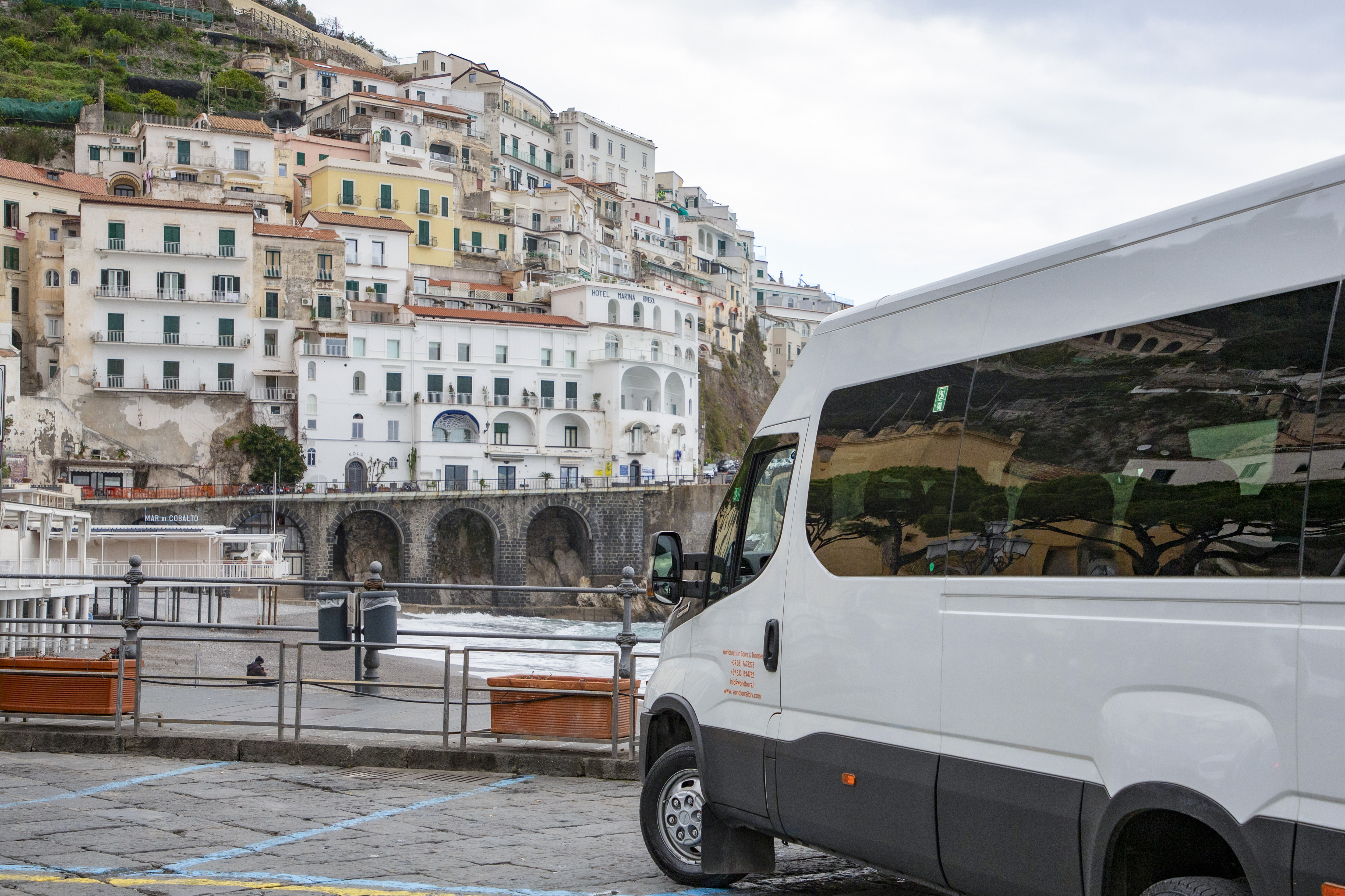 Van parked along the Amalfi Coast with hillside buildings in the background.