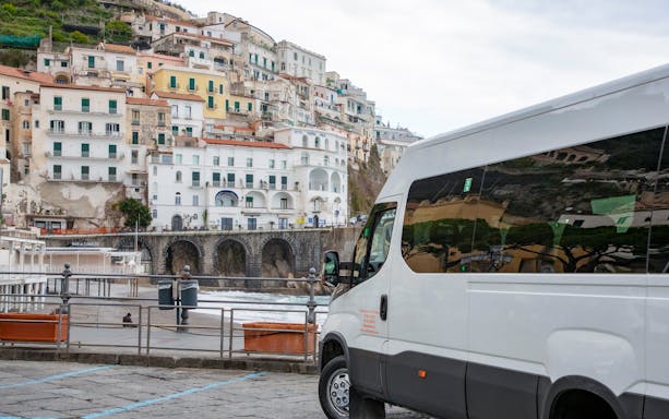 Van parked along the Amalfi Coast with hillside buildings in the background.