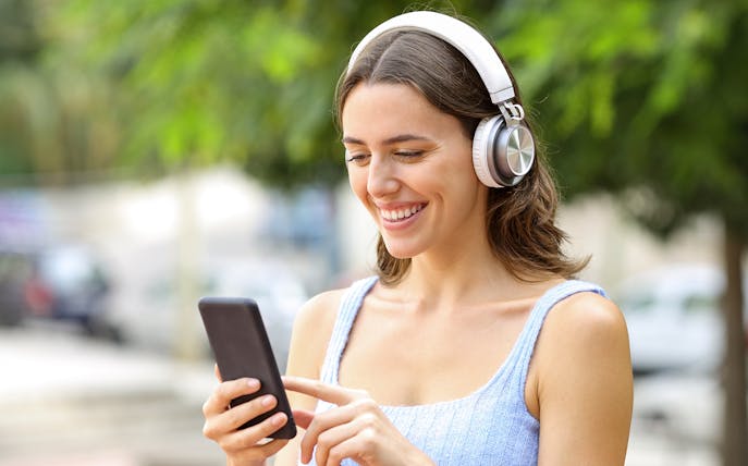 Woman using smartphone audio guide with headphones outdoors.