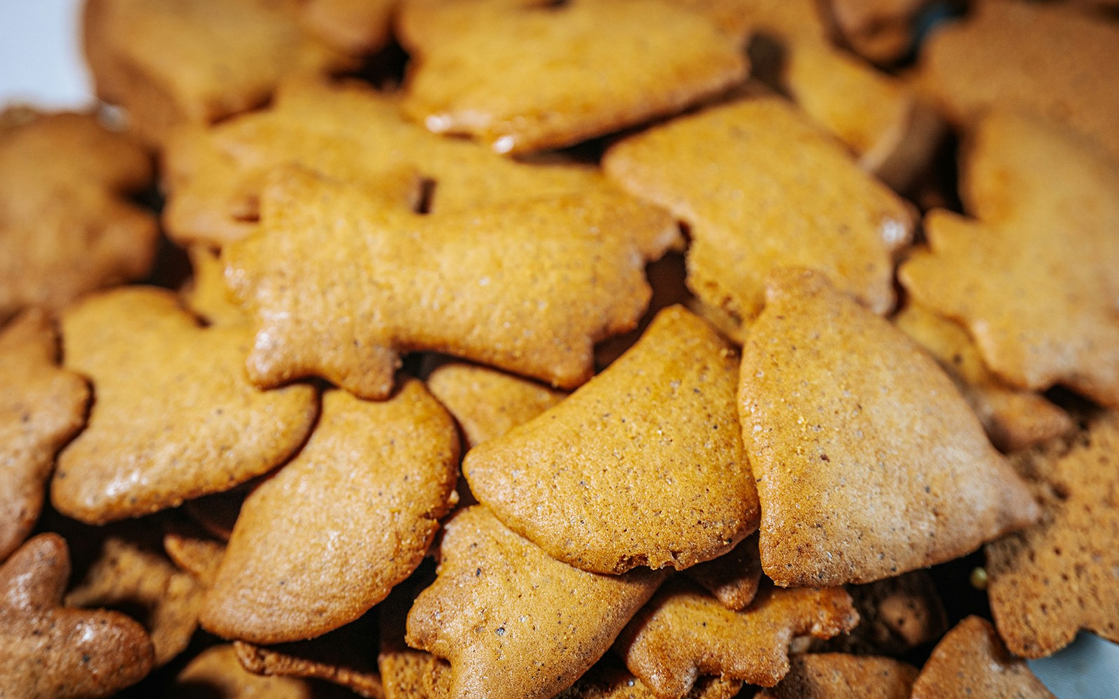 A close-up view of a pile of golden brown gingerbread cookies in various festive shapes, including bells and stars