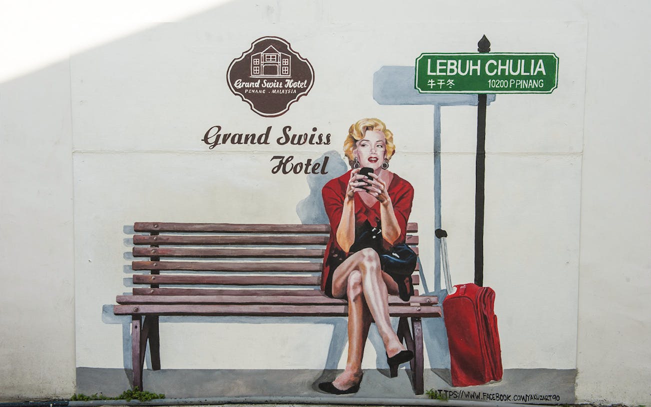 Mural of a woman on a bench with a suitcase at Lebuh Chulia, Penang, near Grand Swiss Hotel.
