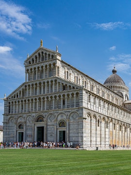 Cathedral of Pisa with tourists outside, featuring its ornate facade and dome.