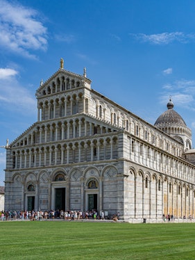 Cathedral of Pisa with tourists outside, featuring its ornate facade and dome.
