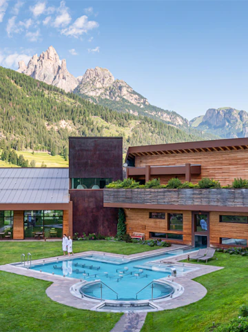 Outdoor pool at QC Terme Dolomiti with mountain view in the background.