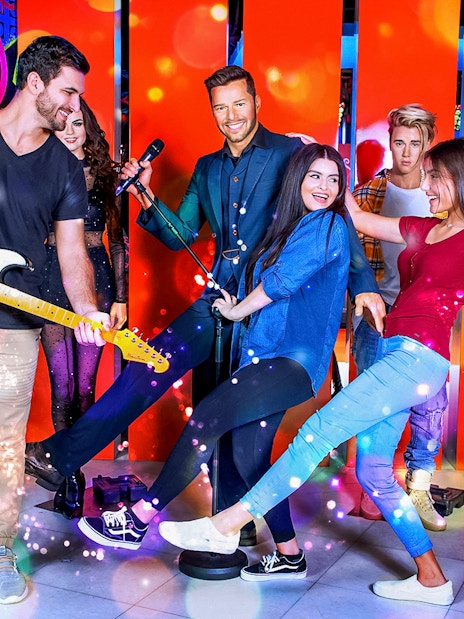 Wax statues of celebrities with visitors at a vibrant museum exhibit.