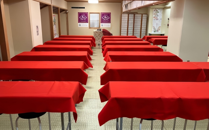Red tables arranged in rows in a room, set up for an audience event.