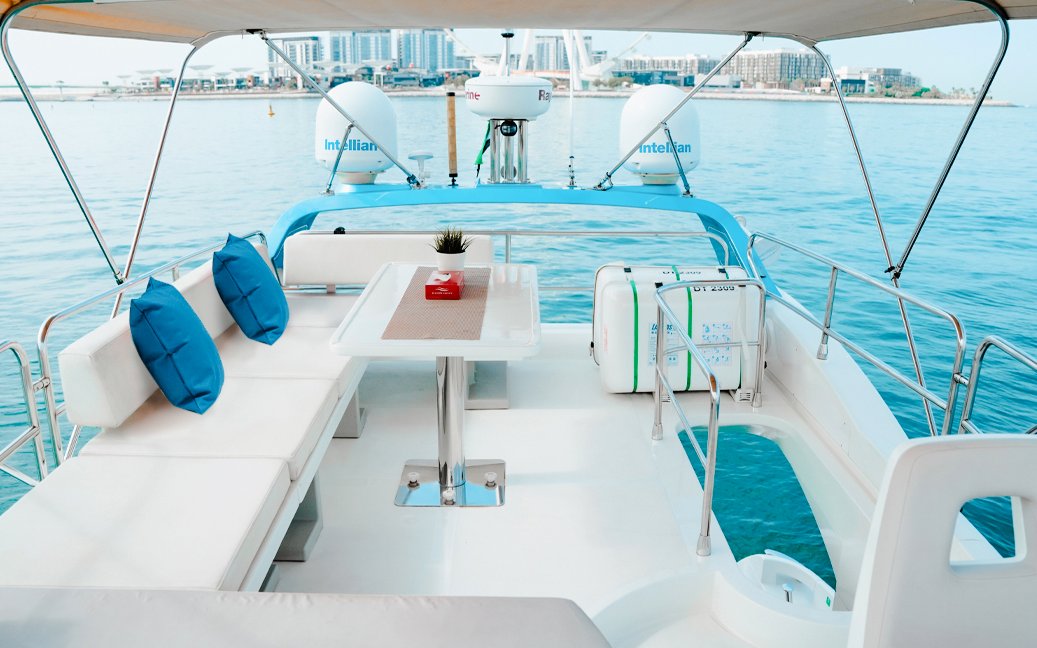 Private luxury yacht deck with seating and table, Dubai Marina in the background.