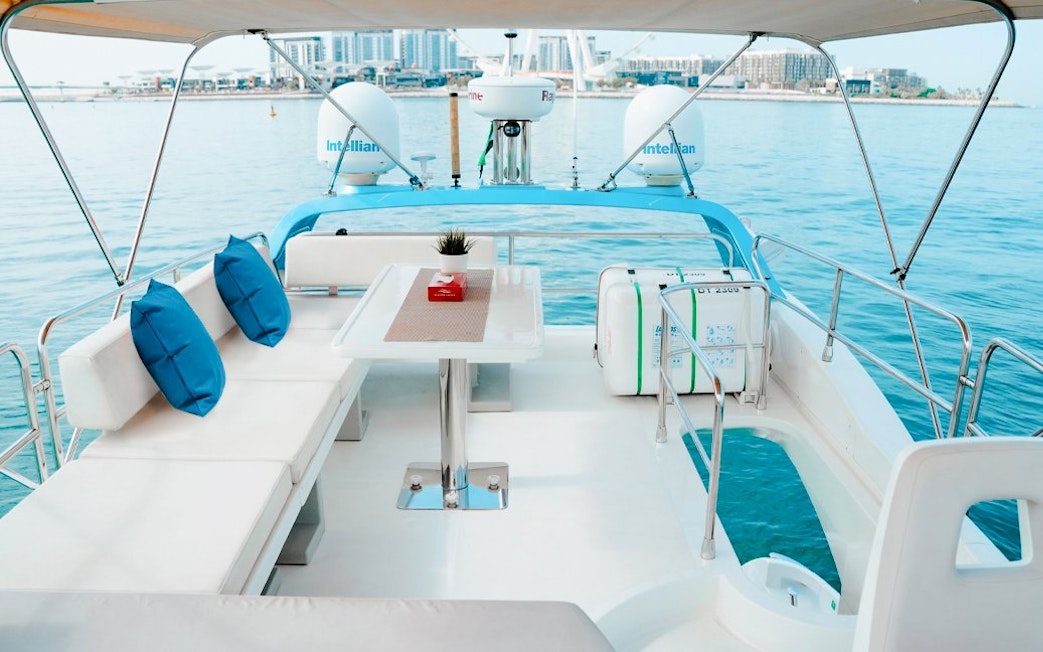Private luxury yacht deck with seating and table, Dubai Marina in the background.