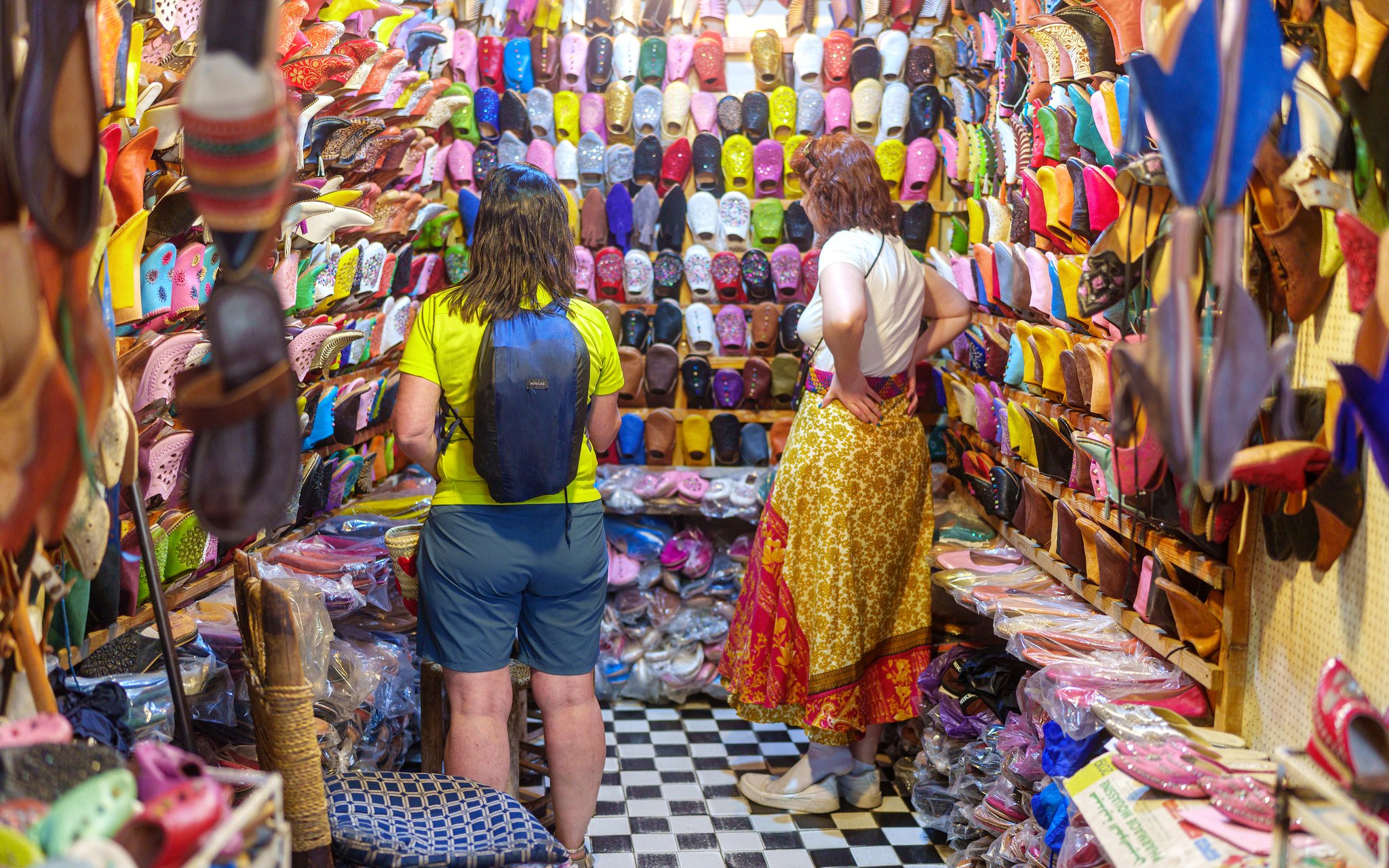 Shoppers browsing colorful slippers in Marrakech souk near Ben Youssef Medersa.
