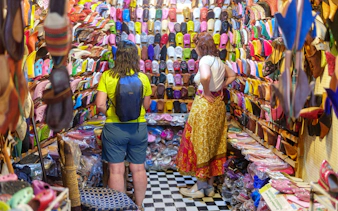Shoppers browsing colorful slippers in Marrakech souk near Ben Youssef Medersa.