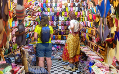 Shoppers browsing colorful slippers in Marrakech souk near Ben Youssef Medersa.