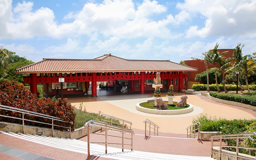 Entrance of Okinawa World with traditional red architecture and lion statues.
