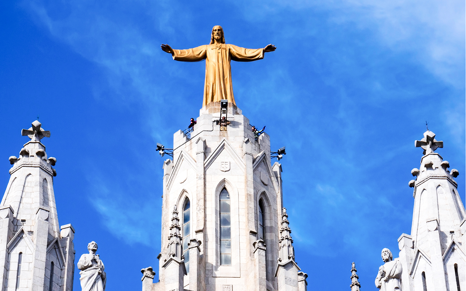 Temple of the Sacred Heart of Jesus statue atop church spire against blue sky.