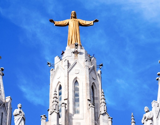 Temple of the Sacred Heart of Jesus statue atop church spire against blue sky.