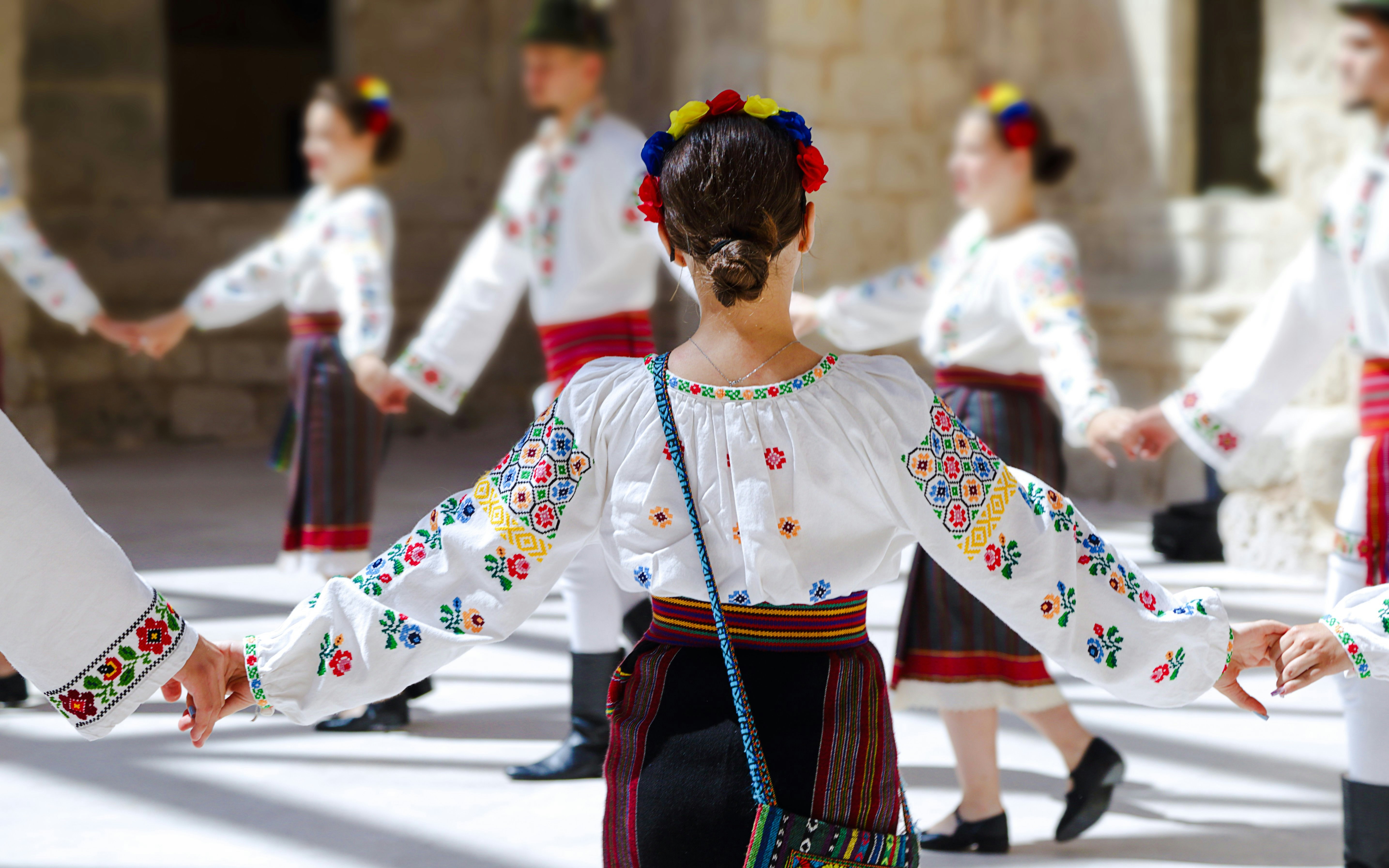 Romanian folk dancers in traditional embroidered costumes performing.