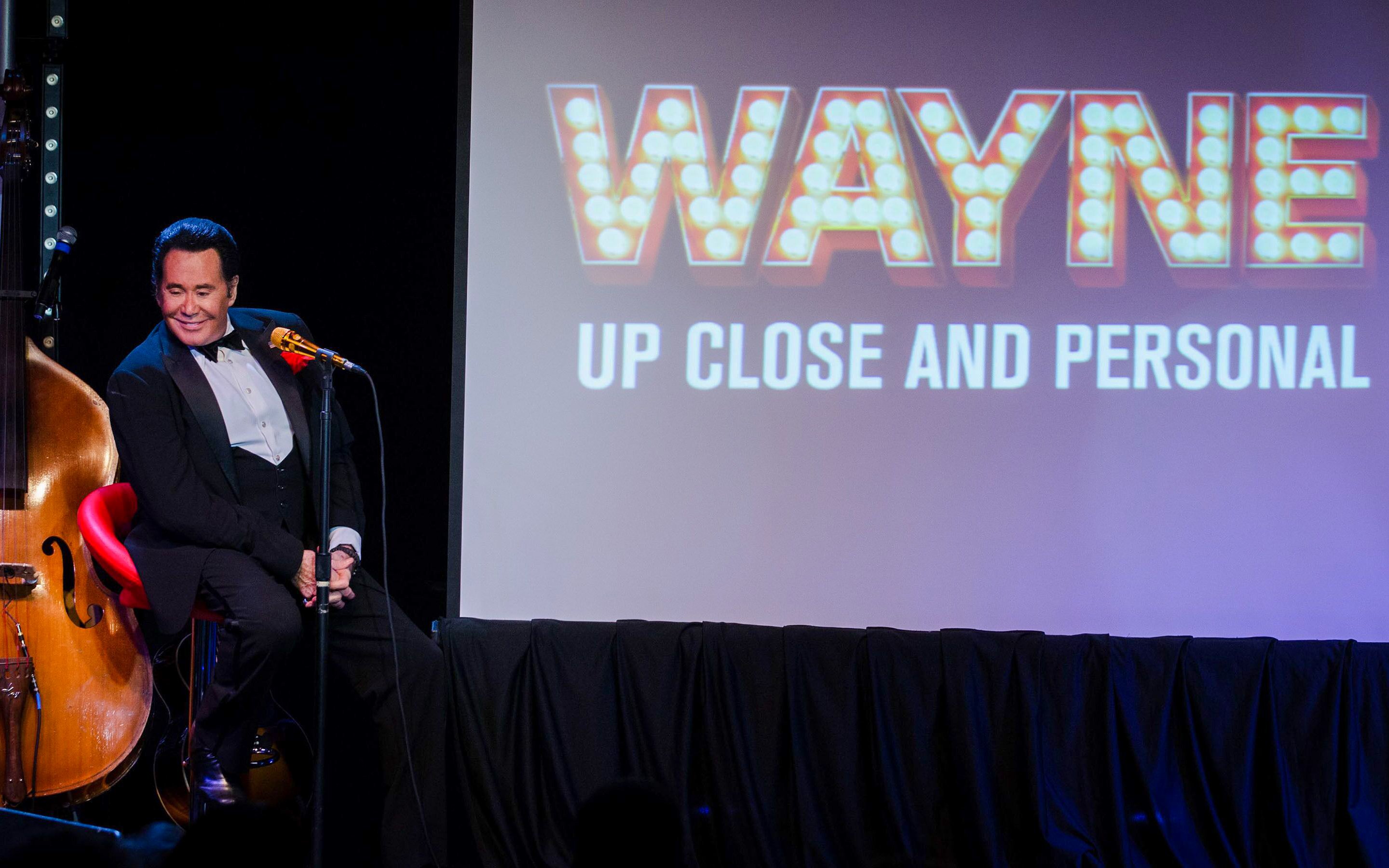 Stage performance of Wayne Newton with "Up Close and Personal" sign in background.