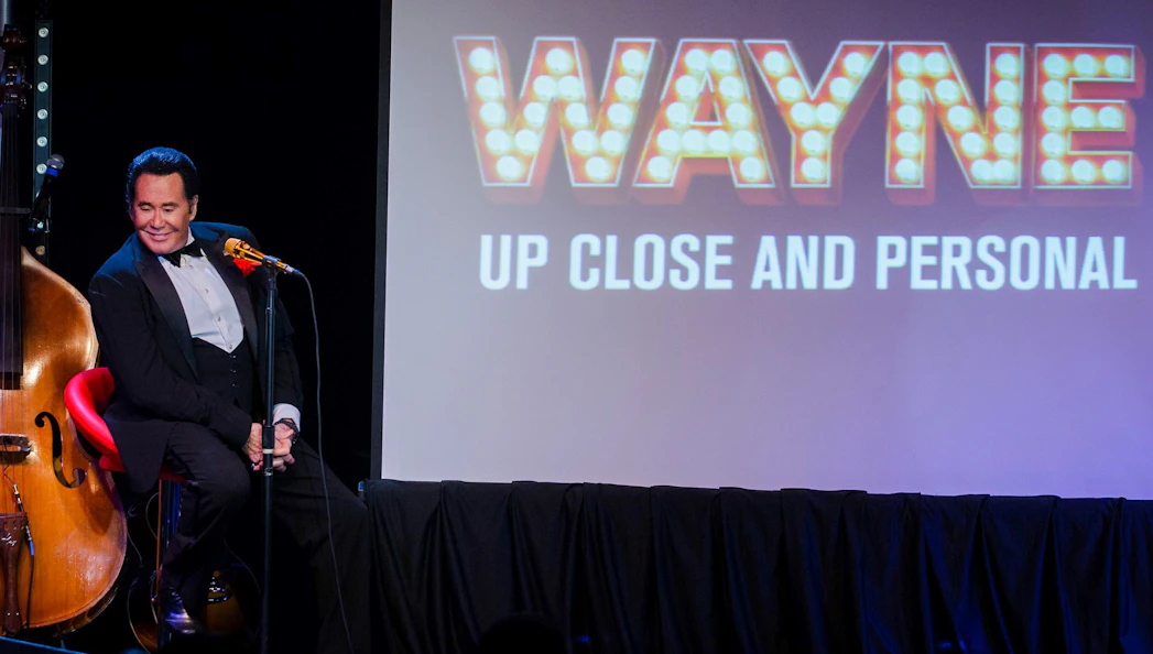 Stage performance of Wayne Newton with "Up Close and Personal" sign in background.