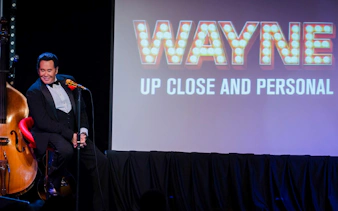 Stage performance of Wayne Newton with "Up Close and Personal" sign in background.