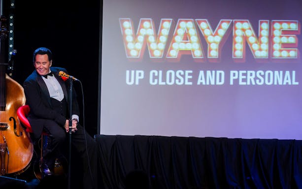Stage performance of Wayne Newton with "Up Close and Personal" sign in background.