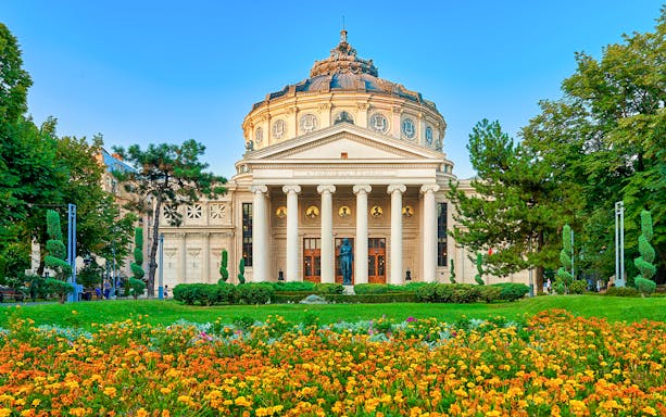 Romanian Athenaeum in Bucharest's Old Town with colorful garden in foreground.
