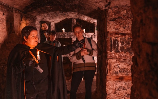 Guide leading a group through an underground passage on a daytime ghost tour.