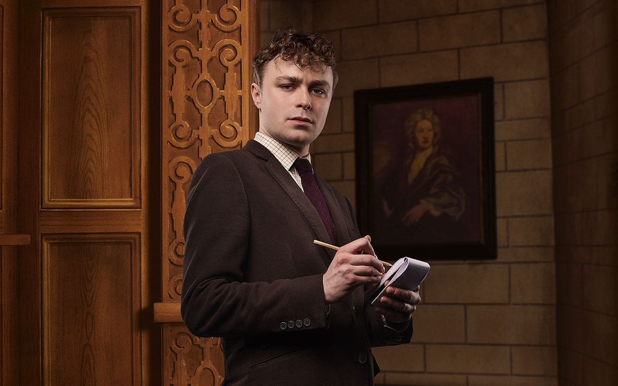 Man in suit taking notes inside a theater setting for The Mousetrap play.